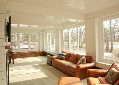 A remodeled sunroom with brown leather couches, natural lighting, and a TV.