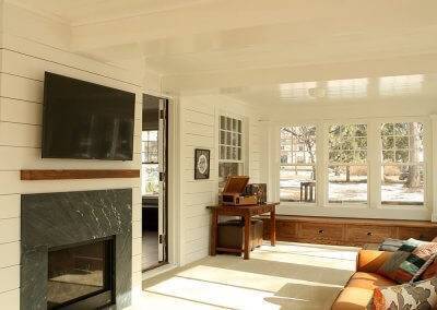 A sunroom with a built-in bench on one end and tan leather couches facing a TV.