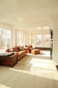 A sunroom with tan leather couches facing a wall with white paneling and a tv mount.