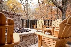 Five adirondack wooden chairs face a built-in firepit on a patio.