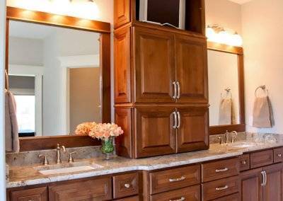 A wide countertop space with two sinks in a bathroom. Wooden cabinetry divides the space between sinks with a small TV.