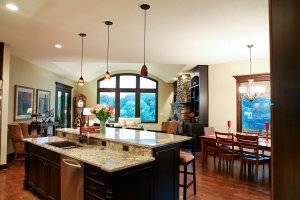 A view of the kitchen and dining room. The kitchen features black cabinetry with a large island and granite countertops.