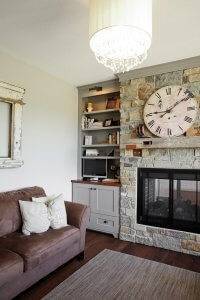 A large fireplace with mixed colors of stone, a brown couch, and large clock on the mantle.