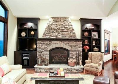 A photo of a stone fireplace in a living room with built-in cabinetry and shelving on either side.