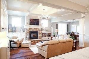 A living room with a stone fireplace, TV, white cabinetry, and sectioned ceiling.