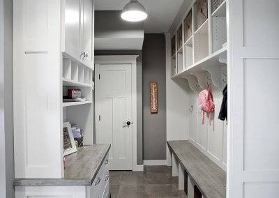 A mudroom bench with hooks and built-in white shelving/cabinetry.