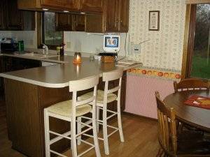 An old outdated kitchen with vintage wallpaper and a tv that is attached to the underside of a cabinet.