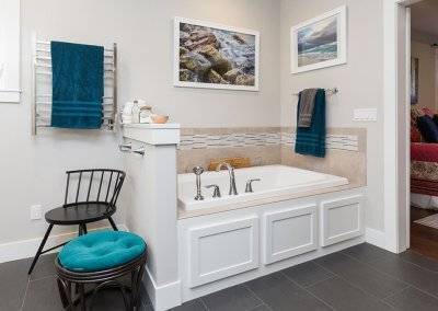A whirlpool bathtub sectioned off in a private corner of a bathroom with blue towels and stool to accent the space.