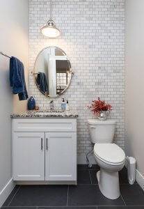 A remodeled half-bathroom with white/gray backsplash on one wall, marbled gray countertops and white cabinets.