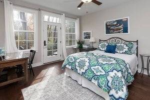 A master bedroom with bed, two desks, and a door leading to a private balcony.