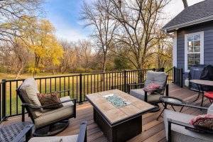 A back patio with four chairs and a fire pit in the center. A view of the backyard beyond the patio.