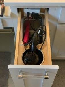 A custom built-in drawer pulls out to reveal space for storage of styling tools such as a hairdryer and hair straightener.