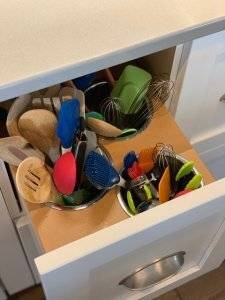 A white drawer pulls out beneath a kitchen counter to reveal built-in crocks to store kitchen utensils.