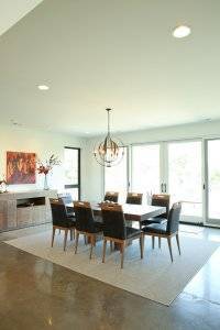 Dining room with table for 8, polished concrete and rug. Double glass doors open to backyard patio and outdoor kitchen.