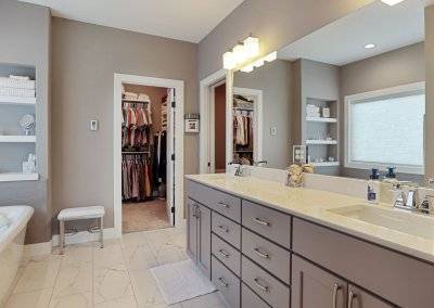 Master bathroom with dual sinks, built in shelving over bathtub, tile floor and walk in closet.