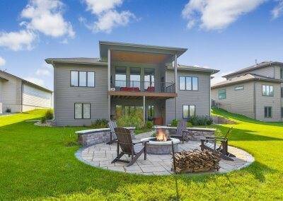 Rear exterior photo showing fire pit, circular patio, covered deck and adjacent homes.