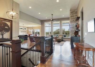 Great room view from the entry featuring floor to ceiling windows, stone fireplace and stairwell.