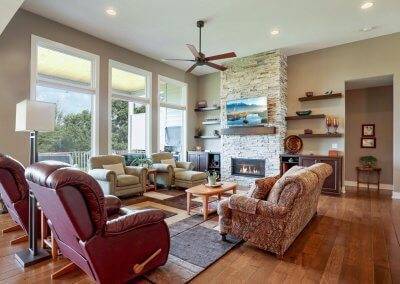 Great room with large windows, stone fireplace and floating shelves.