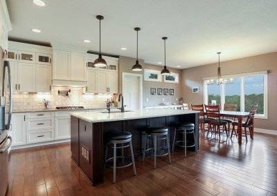 Kitchen with island, pendant lighting, hardwood floors, white tile backsplash, pot filler and glass front cupboards.
