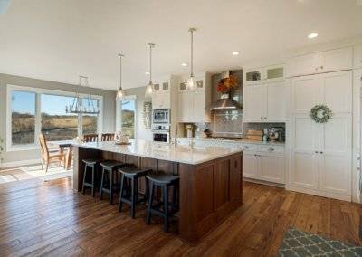 White kitchen with hardwood flooring, hidden pantry, island and dining table.