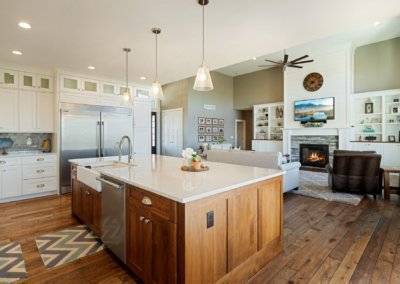 Open view of kitchen and living area featuring hardwood flooring, stone fireplace and quartz counter top island.