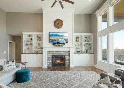 Great room space with stone fireplace, shiplap, built in cabinetry and large windows.