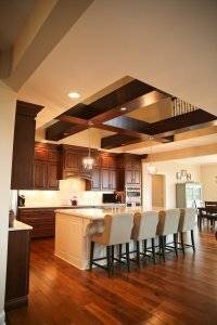 Two story kitchen design with open ceiling, beams, hardwood flooring and island seating.