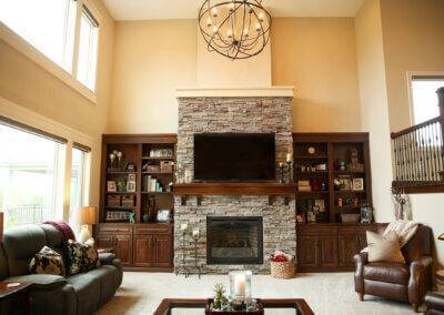 two story family room with stair railing, stone fireplace, custom shelving and windows.
